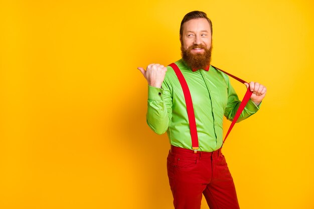 Zdjęcie atrakcyjnego fajnego faceta funky wygląd bezpośredni palec puste miejsce doradztwo sprzedaż zakupy nosić zieloną koszulę czerwoną muszkę szelki spodnie na białym tle żółty kolor