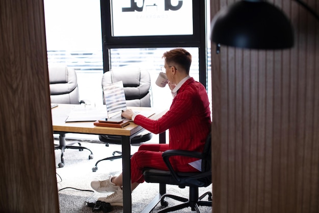 Zdjęcie atrakcyjnej dojrzałej bizneswoman w czerwonym garniturze pracującej na laptopie na swoim stanowisku pracy
