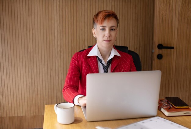 Zdjęcie atrakcyjnej dojrzałej bizneswoman w czerwonym garniturze pracującej na laptopie w swoim biurze