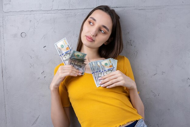 Zdjęcie bogatej kobiety w prostych ubraniach trzymającej wachlarz dolarowych pieniędzy na tle betonowej ściany