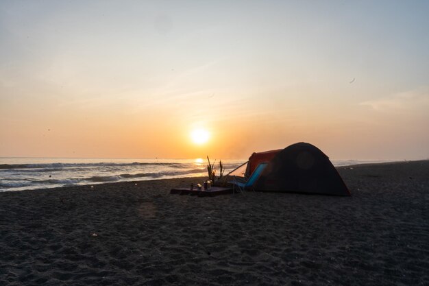 Zdjęcie czerwonego namiotu kempingowego na plaży o zachodzie słońca autorstwa Yuri Ugarte Cespedes