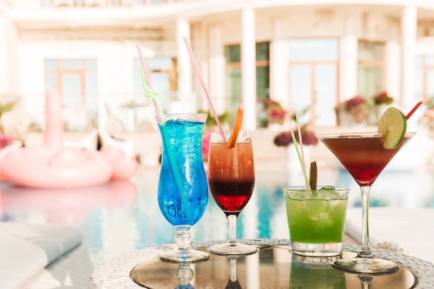 Zdjęcie czterech koktajli w szklankach przy stole w pobliżu hotelowego basenu, w słoneczny letni dzień