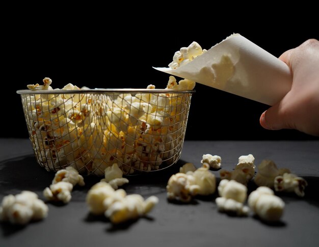 Zdjęcie domowego popcornu w białym papierowym rożku z metalowym koszem na czarnym tle