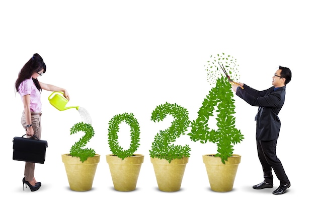 Zdjęcie dwóch młodych pracowników tnących i podlewających drzewo w kształcie numeru 2024 na białym tle Koncepcja inwestycji biznesowych na 2024 rok