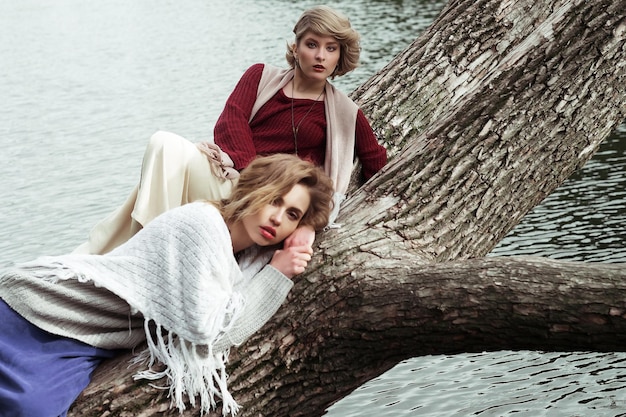 Zdjęcie dwóch pięknych kobiet pozujących na drzewie w pobliżu jeziora