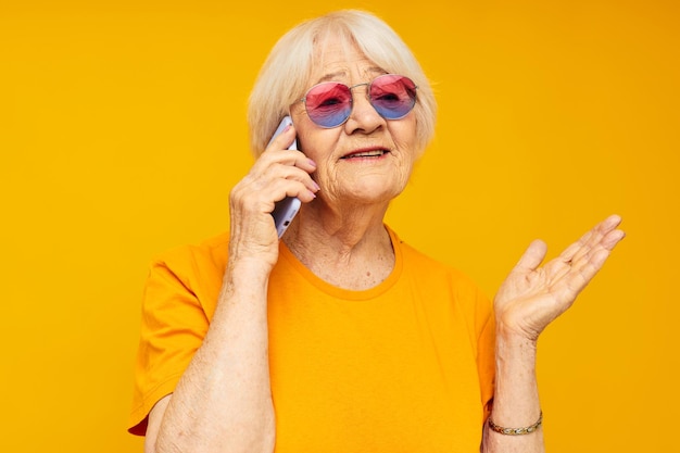 Zdjęcie emerytowanej starszej pani rozmawiającej przez telefon w żółtych okularach na żółtym tle