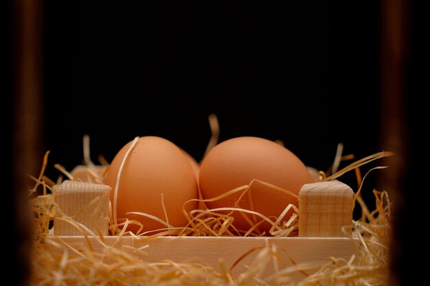 Zdjęcie zdjęcie jaj ekologicznych w drewnianym pojemniku otoczonym słomą na czarnym tle