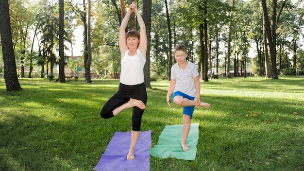 Zdjęcie Kobiety W średnim Wieku Uczy Swojego Ucznia W Zajęciach Jogi W Parku. Woamn Z Nastoletnim Chłopcem ćwiczącym Fitness, Medytację I Jogę Na Trawie W Lesie