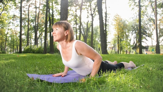 Zdjęcie kobiety w średnim wieku uprawiania jogi lub fitness na świeżej zielonej trawie w parku. Zdrowie fizyczne i psychiczne kobiet. Osoba w medytacji i harmonii ciała i duszy