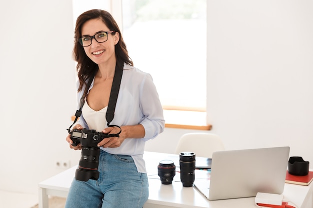 Zdjęcie kobiety wesoły pozytywny optymistyczny młody fotograf w biurze z aparatem.