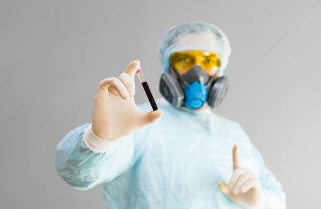 Zdjęcie lekarza w odzieży ochronnej trzyma probówkę z próbką zakażonej krwi w jego