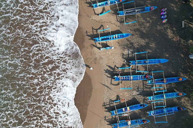 zdjęcie lotnicze niebieskich łodzi rybackich zakotwiczonych na czarnej, piaszczystej plaży. turystyka. pejzaż morski. fale.