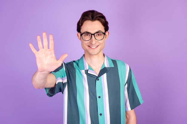 Zdjęcie młodego wesołego mężczyzny w dobrym nastroju fala ramię witam symbol okulary na białym tle nad fioletowym kolorem tła