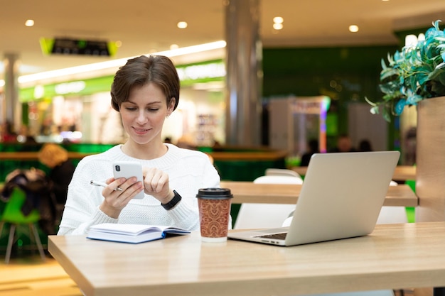 Zdjęcie młodej atrakcyjnej brunetki siedzącej w centrum handlowym przy stole z papierem do kawy