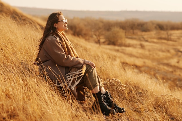 Zdjęcie młodej kobiety siedzącej na zachodzie słońca w polu, światło słoneczne, relaks