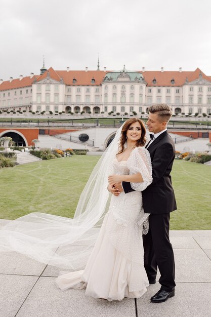 Zdjęcie młodej pary w sukni ślubnej, stojąc w uścisku na tle europejskiego starego miasta, uśmiechając się i patrząc na kamery. Dzień ślubu