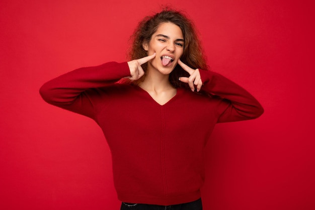 Zdjęcie młodej pozytywnej szczęśliwej pięknej brunetki kręcone kobiety ze szczerymi emocjami na sobie dorywczo czerwony sweter na białym tle na czerwonym tle z miejsca kopiowania i pokazując zabarwienie.
