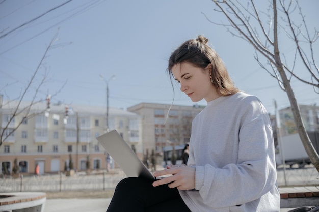 Zdjęcie modnej uroczej młodej kobiety siedzącej w pobliżu fontanny w przerwie od pracy wygląda na laptop