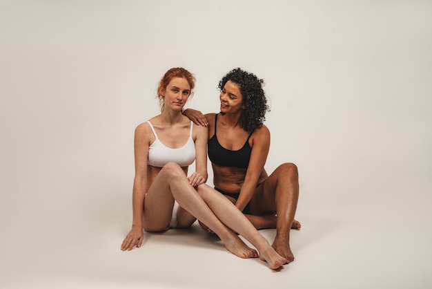 Zdjęcie naturalnych wielorasowych kobiet, pozytywne na ciele. Feministyczne kobiety w bieliźnie siedzą, na białym tle. Koncepcja naturalnego piękna i siły dziewczyny.