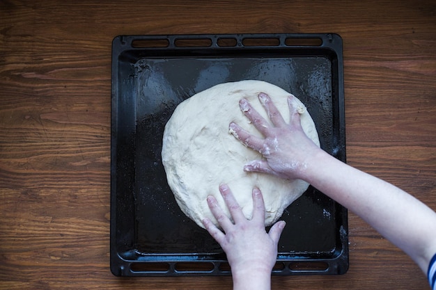 Zdjęcie osoby rozciągającej ciasto na pizzę na blasze do pieczenia z widoku z góry piekarnika