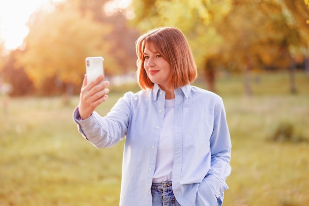 Zdjęcie oszałamiającej pozytywnej falistej fryzury sprawia, że selfie nagrywa wideo wieczorem ulica o zachodzie słońca