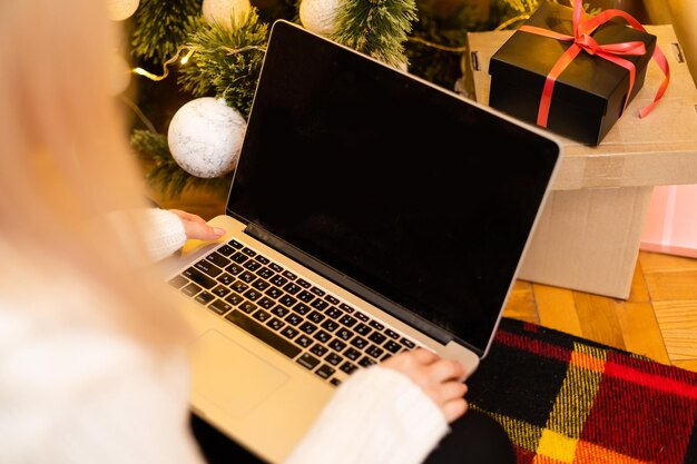 Zdjęcie pięknej blond kobiety siedzącej na kanapie za pomocą laptopa, aby kupić prezenty świąteczne.