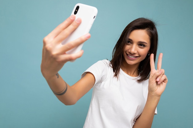 Zdjęcie Pięknej Uśmiechniętej Szczęśliwej Młodej Brunetki Ubranej W Dorywczo Białą Koszulkę Odizolowaną Nad ścianą