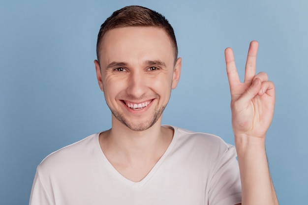 Zdjęcie portret mężczyzny pozytywnego, ładnego pokazującego gest v-sign uśmiechnięty na tle pastelowego niebieskiego koloru