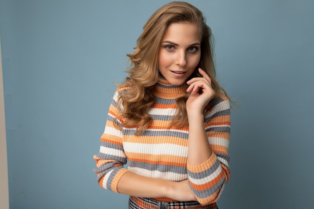 Zdjęcie portret młodej pięknej pozytywnej seksownej zamyślonej blondynki ze szczerymi emocjami na sobie pasiasty sweter na białym tle na niebieskim tle z miejsca kopiowania i myślenia.