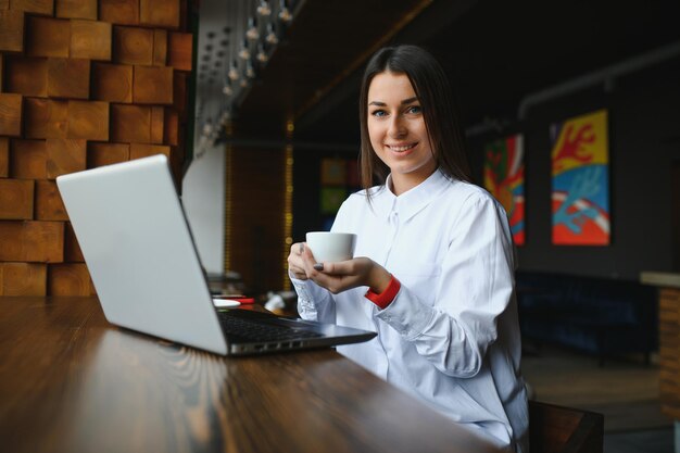 Zdjęcie portret wspaniałej atrakcyjnej kobiety pracującej na laptopie, piszącej na maszynie, siedząc w kawiarni, pijąc kawę