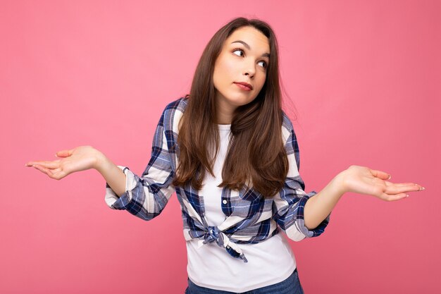 Zdjęcie portretowe młodej zamyślonej pięknej brunetki kobiety ze szczerymi emocjami na sobie stylową koszulę w kratkę na białym tle na różowym tle z miejsca na kopię i mającą wątpliwości.