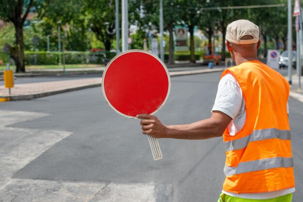 Zdjęcie pracownika budowlanego trzymającego czerwony znak stopu i kierującego ruchem na ulicy