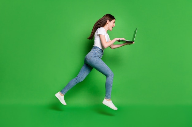 Zdjęcie profilowe na całej długości szalonej dziewczyny jump run używać laptopa nosić t-shirt denim na białym tle na zielonym tle