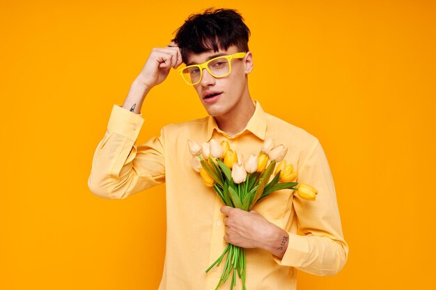 Zdjęcie romantycznego młodego chłopaka w żółtych okularach z bukietem kwiatów niezmieniony styl życia