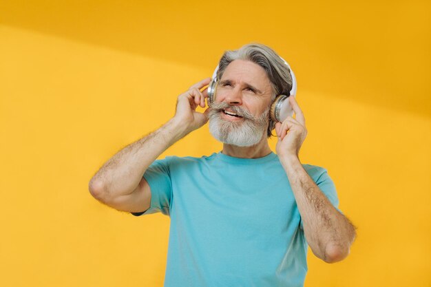 Zdjęcie siwego starszego mężczyzny w słuchawkach śpiewających na żółtym tle
