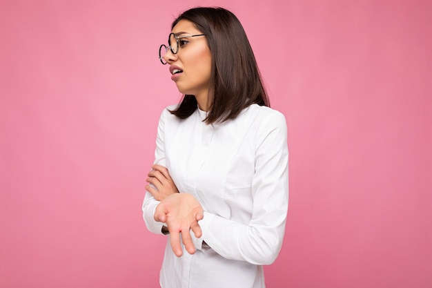 Zdjęcie strzał pięknej zmęczonej młodej kobiety brunetka ubrana w zwykłe ubrania i stylowe okulary optyczne na białym tle nad kolorowym tłem, patrząc z boku.