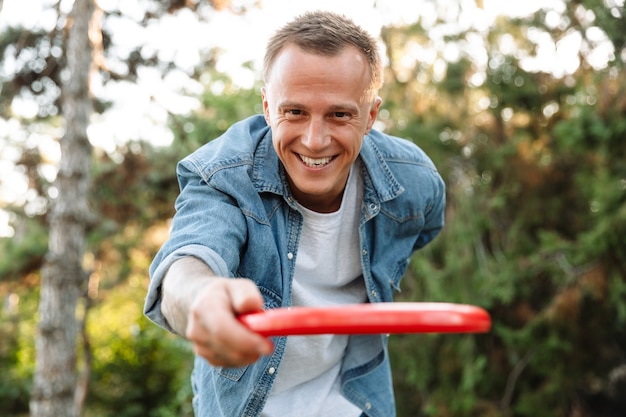 Zdjęcie Szczęśliwego Młodego Przystojnego Mężczyzny śmiejącego Się I Rzucającego Latającym Dyskiem Podczas Gry We Frisbee W Parku