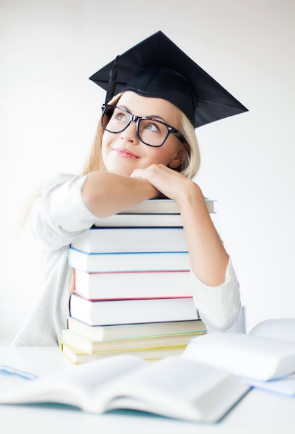 zdjęcie szczęśliwego studenta w czapce dyplomowej ze stosem książek