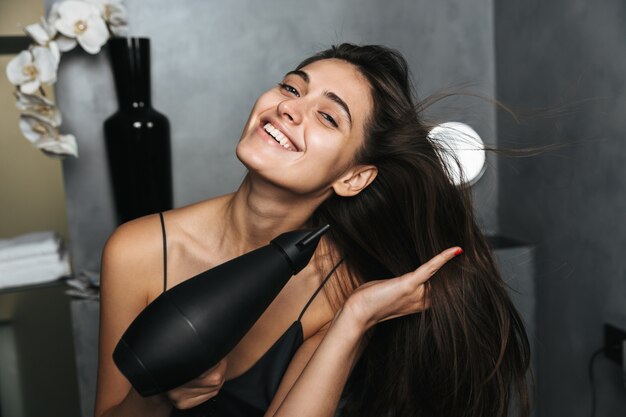 Zdjęcie szczęśliwej kobiety o długich ciemnych włosach i zdrowej skórze suszącej włosy