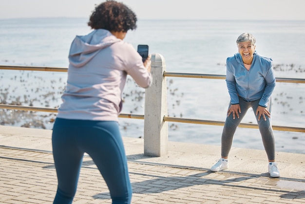 Zdjęcie telefoniczne i przyjaciele śmieją się ze starszych kobiet na plaży z zabawnym żartem na morzu dla fitnessu Ćwicz telefon komórkowy i zdjęcie do postu w mediach społecznościowych na spacerze promenadą oceaniczną na trening i przyjaźń