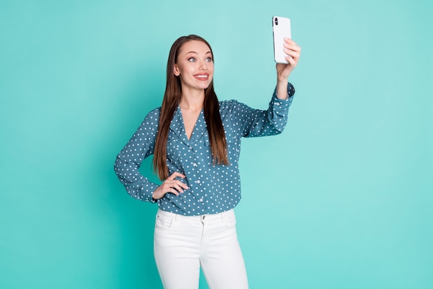 Zdjęcie uroczej, dobrze wyglądającej dziewczyny robi selfie na telefonie komórkowym na białym tle nad turkusowym kolorem tła