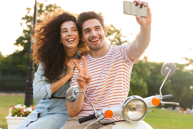 Zdjęcie uroczej pary przy selfie na telefon komórkowy, siedząc razem na skuterze w parku miejskim