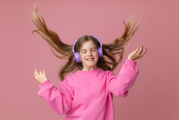 Zdjęcie uroczej, zabawnej młodej nastolatki w różowych słuchawkach skoczka tańczącej, cieszącej się muzyką na tle