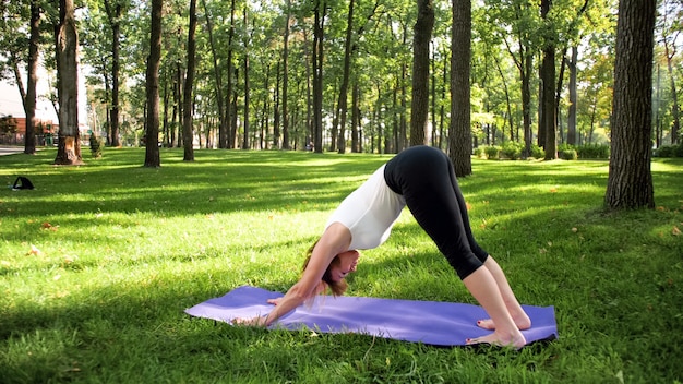 Zdjęcie uśmiechnięta szczęśliwa kobieta 40 lat robi ćwiczenia jogi na macie fitness w lesie. Harmonia człowieka w naturze. Osoby w średnim wieku dbające o zdrowie psychiczne i fizyczne