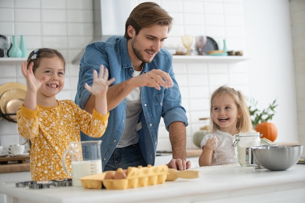 Zdjęcie uśmiechniętego ojca i córek pieczenia w kuchni i zabawy.