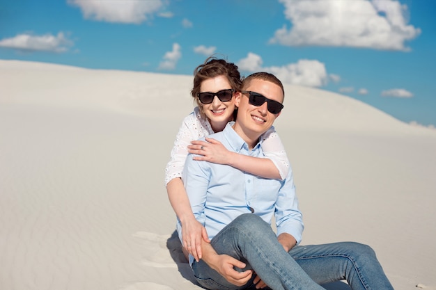 Zdjęcie wspaniałej pary mężczyzny i kobiety, uśmiechając się i przytulanie na piaszczystym wzgórzu.
