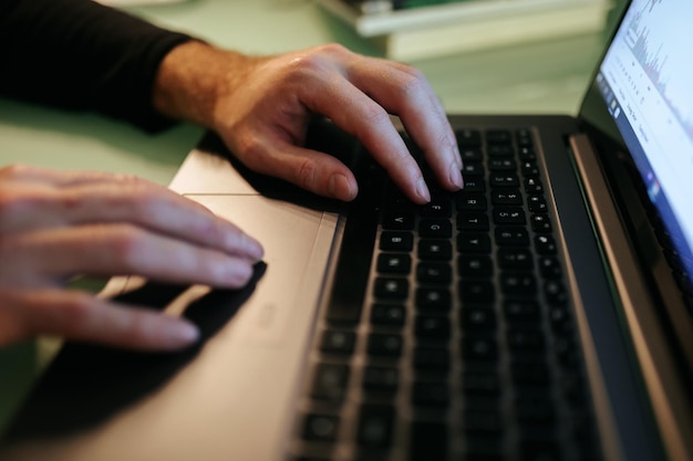 Zdjęcie z bliska pary rąk piszących na laptopie oświetlonym przez blask ekranu w