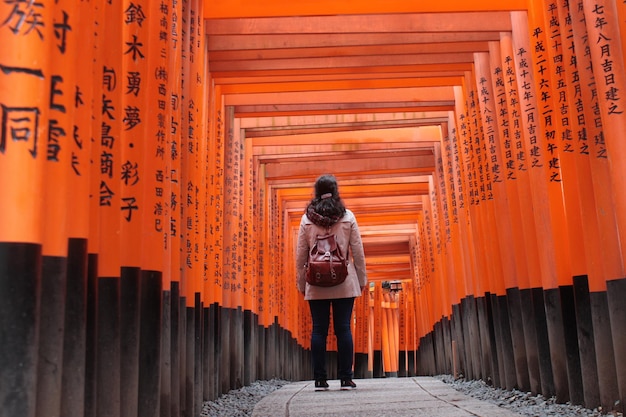 Zdjęcie z tyłu kobiety stojącej pośród bram torii w świątyni fushimi inari