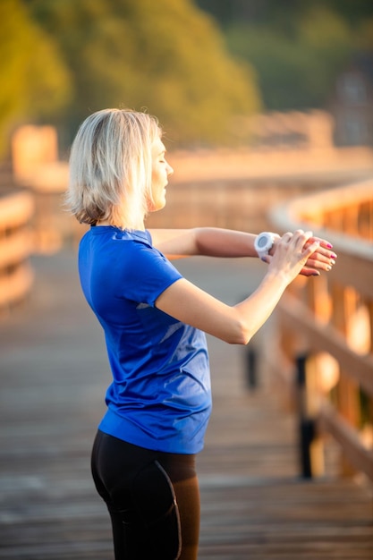 Zdjęcie z tyłu wysportowana kobieta patrzy na zegar pod ręką stojący na drewnianym moście w parku w letni dzień
