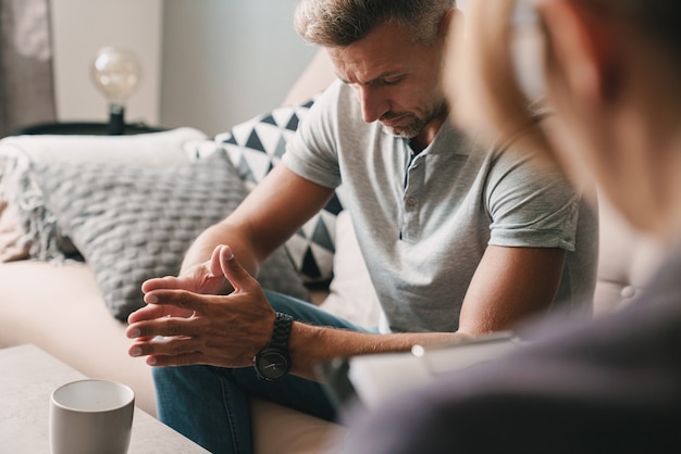 Zdjęcie zamyślonego, skoncentrowanego mężczyzny rozmawiającego z psychologiem podczas sesji terapeutycznej w pokoju